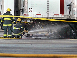 Firefighters hose down wreckage from the plane, which came to rest under a tractor<br />trailer.