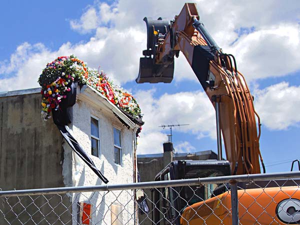 A claw truck sits beside 3711 Melon Street in anticipation of its demolition. The home is dressed with a flower crown for its "funeral" which occured on May 31st. Hundreds of Mantua residents attended the ceremony which was officiated by Pastor Harry Moore Senior from the Mount Olive Baptist Church. (RACHEL WISNIEWSKI / Staff Photographer)