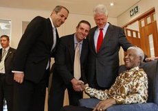 During a trip to South Africa, Roger Band shakes hands with Nelson Mandela as brother Douglas and Bill Clinton look on.