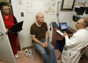 Allan Crimm, a Center City physician, uses a laptop to chart information as he meets with patient Sean Falls. Holding her laptop in the doorway is medical assistant Lily Cruz. Crimm says he needs resources for a more proactive approach to care.