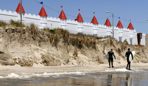 Surfers heading to a competition in Ocean City, N.J., pass a wall of sand that was a barrier dune before Monday's storm. Shore damage varied widely.