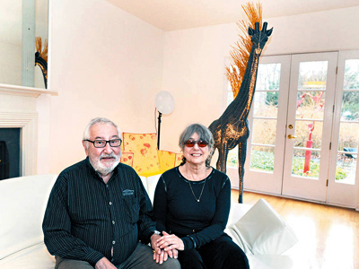 Warren and Dolores Browne in their living room in Merion Station. Behind them is the glass beaded giraffe that got from the Dali Museum. ( Sharon Gekoski-Kimmel / Staff Photographer )  