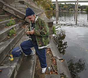 John Zaharchuk baits his hook to fish in the Schuylkill in East Falls. Now 59, he’s not sure whether he lived on the streets for 10 years or for 15 years.<br />