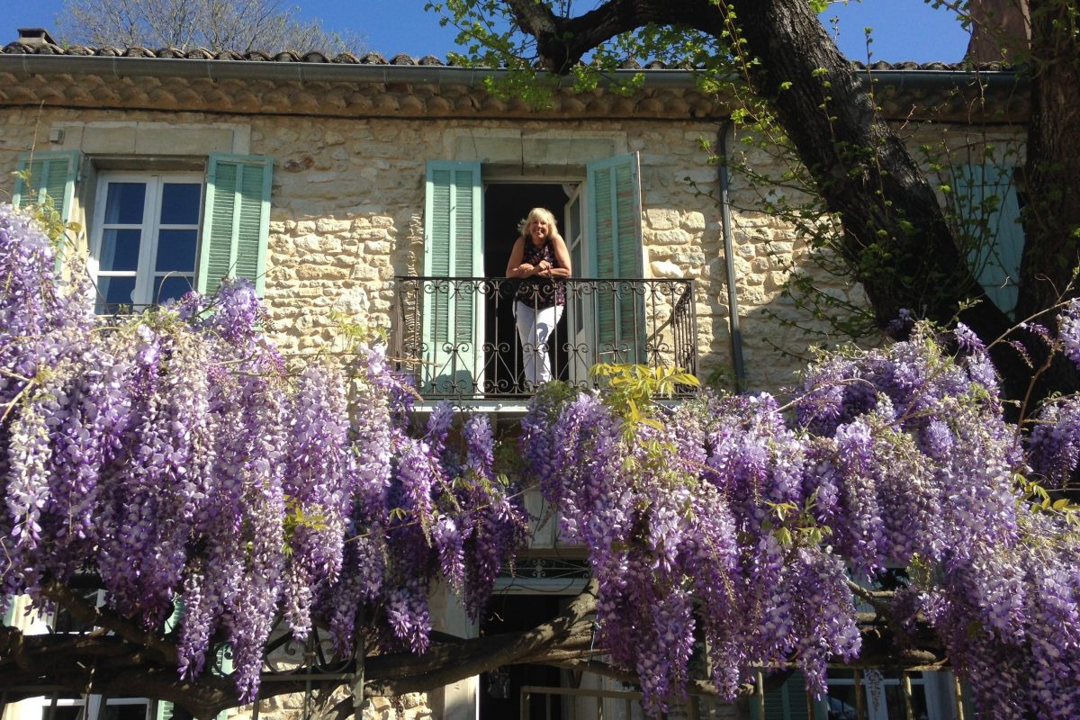 Owner Trish Michie stands on the balcony at Maison Noel in Lagnes, France, with the wisteria in full bloom. 